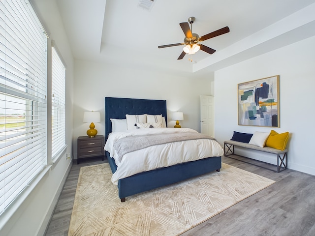 bedroom with ceiling fan, hardwood / wood-style flooring, a tray ceiling, and multiple windows