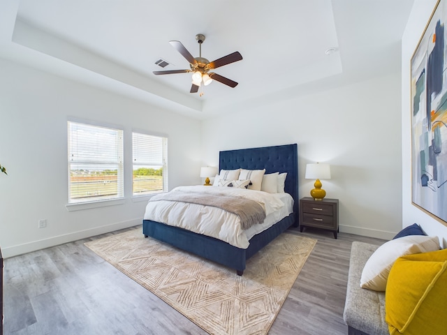 bedroom featuring wood-type flooring, ceiling fan, and a raised ceiling