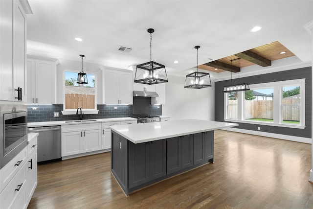 kitchen with beamed ceiling, appliances with stainless steel finishes, white cabinetry, and a kitchen island