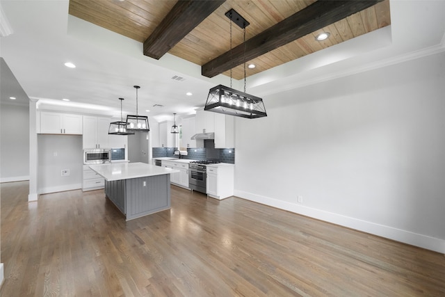 kitchen featuring appliances with stainless steel finishes, pendant lighting, white cabinets, hardwood / wood-style floors, and a kitchen island