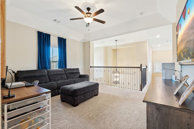 carpeted living room featuring ceiling fan with notable chandelier and a tray ceiling