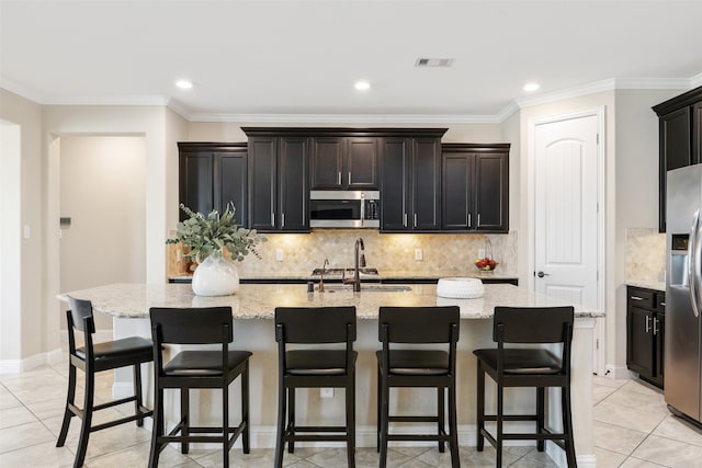 kitchen featuring light stone countertops, an island with sink, stainless steel appliances, and ornamental molding