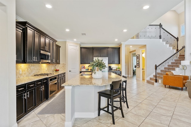 kitchen featuring appliances with stainless steel finishes, light stone counters, a breakfast bar, crown molding, and a center island