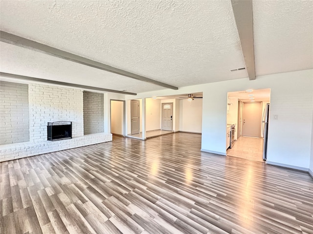 unfurnished living room with ceiling fan, beam ceiling, a brick fireplace, wood-type flooring, and a textured ceiling