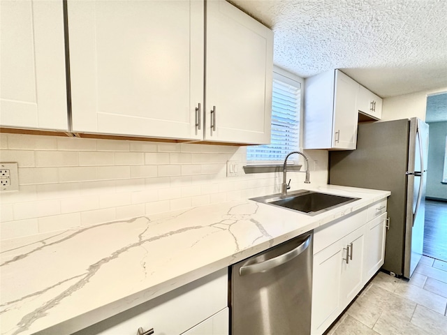 kitchen featuring appliances with stainless steel finishes, white cabinetry, light stone counters, a textured ceiling, and sink