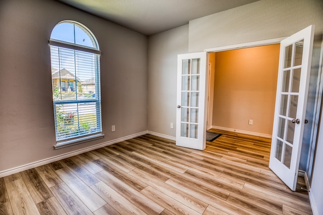 empty room featuring french doors, light hardwood / wood-style flooring, and a wealth of natural light