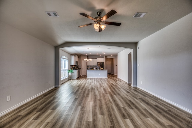 unfurnished living room with a textured ceiling, ceiling fan with notable chandelier, vaulted ceiling, and dark wood-type flooring