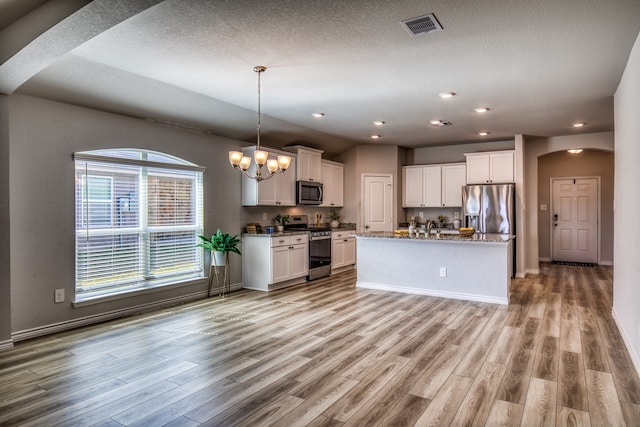 kitchen featuring appliances with stainless steel finishes, light hardwood / wood-style floors, white cabinets, a kitchen island with sink, and a notable chandelier