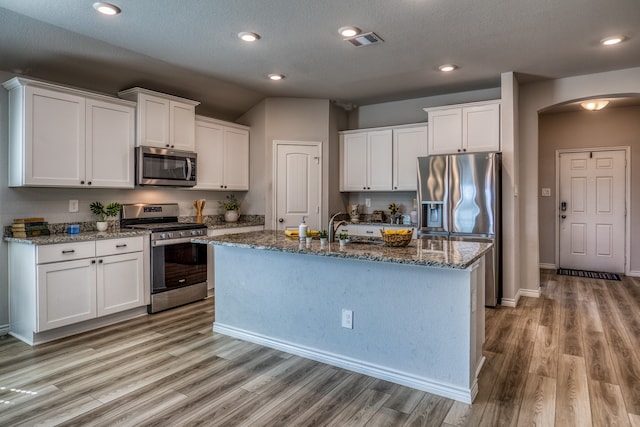 kitchen featuring white cabinetry, a center island with sink, appliances with stainless steel finishes, and light hardwood / wood-style floors