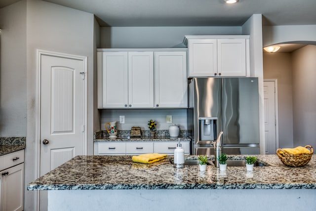 kitchen with dark stone countertops, white cabinets, sink, and stainless steel fridge with ice dispenser