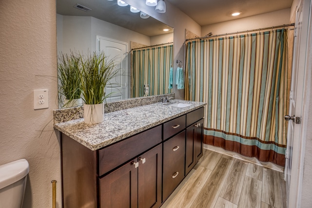 full bathroom with hardwood / wood-style floors, shower / tub combo with curtain, vanity, and toilet