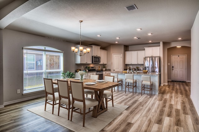 dining space with a textured ceiling, light hardwood / wood-style flooring, sink, and a chandelier