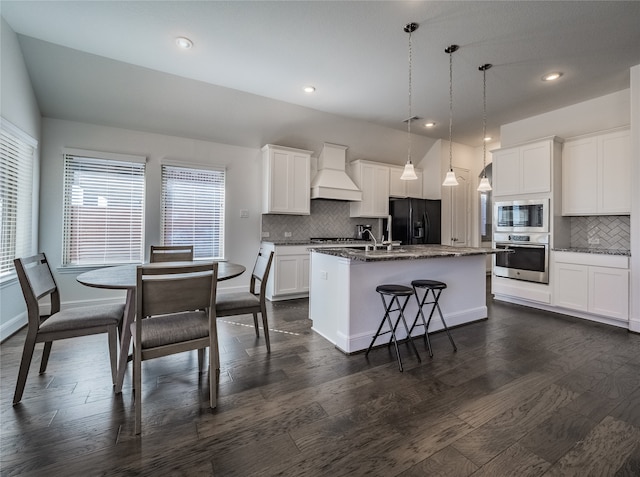 kitchen with dark hardwood / wood-style flooring, stainless steel appliances, a center island with sink, and custom exhaust hood