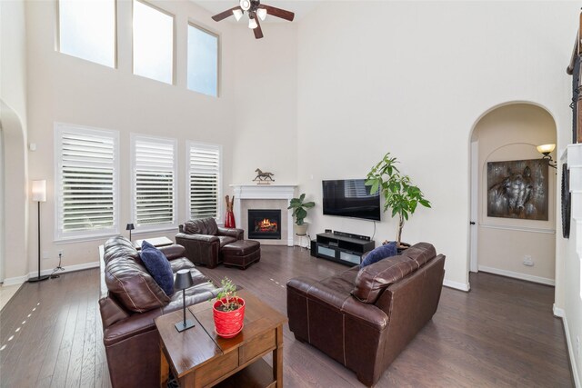 living room featuring a towering ceiling, a fireplace, ceiling fan, and dark hardwood / wood-style flooring