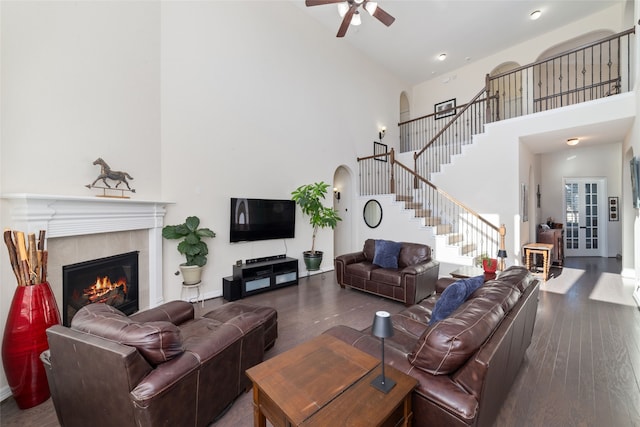 living room with a tiled fireplace, ceiling fan, a high ceiling, and wood-type flooring