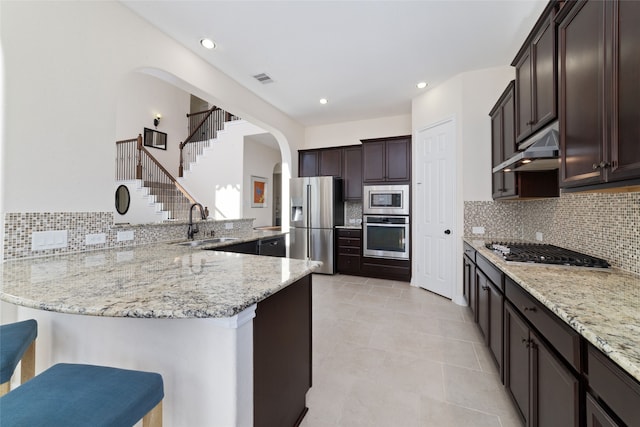 kitchen with a kitchen breakfast bar, stainless steel appliances, kitchen peninsula, light stone counters, and tasteful backsplash