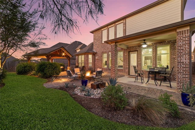 back house at dusk with a yard, an outdoor fire pit, a patio area, and a gazebo