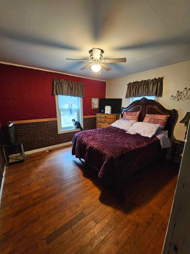 bedroom featuring dark hardwood / wood-style flooring, ceiling fan, and brick wall