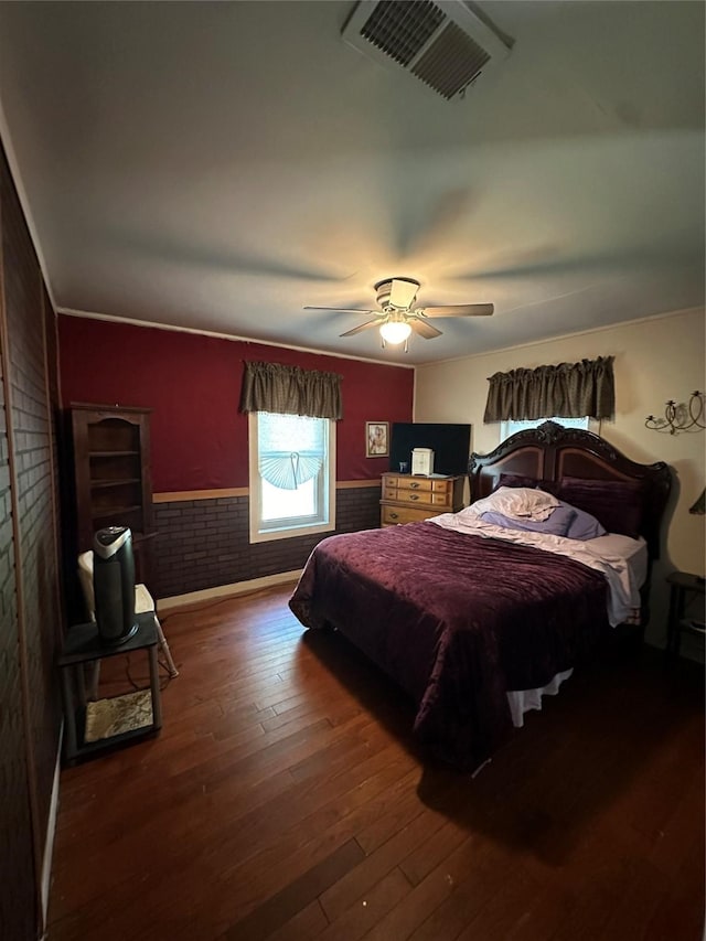 bedroom with dark hardwood / wood-style floors, ceiling fan, and brick wall