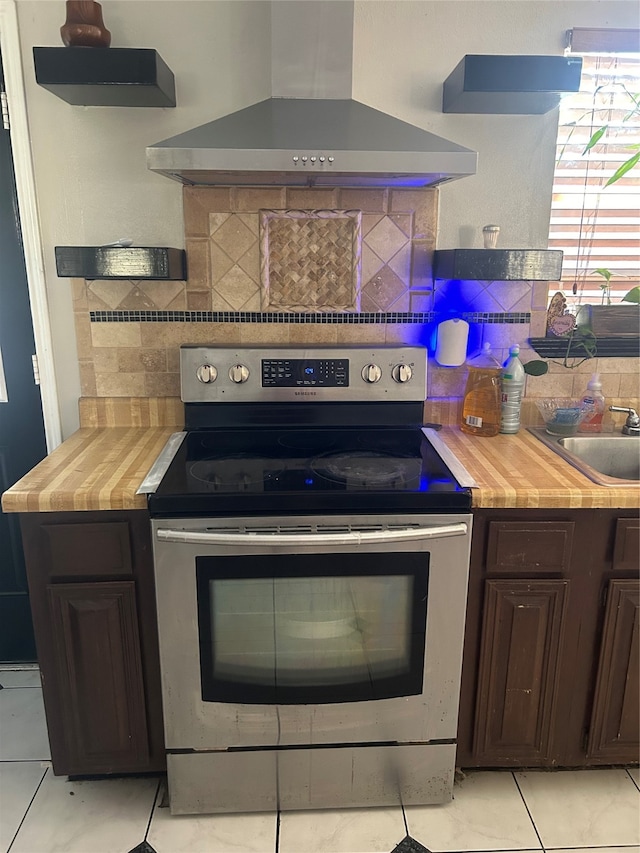 kitchen featuring stainless steel range with electric cooktop, dark brown cabinetry, wall chimney exhaust hood, and wooden counters