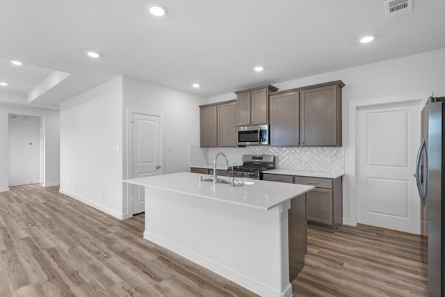 kitchen with appliances with stainless steel finishes, sink, light hardwood / wood-style flooring, and an island with sink