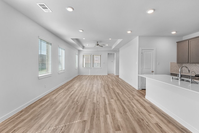 unfurnished living room featuring a wealth of natural light, sink, ceiling fan, and light hardwood / wood-style flooring