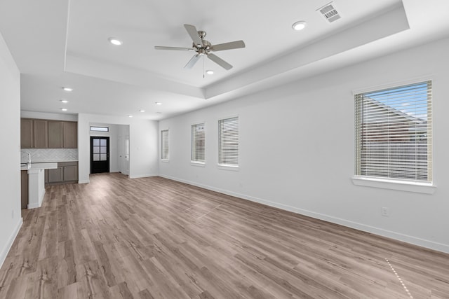 unfurnished living room with ceiling fan, light hardwood / wood-style flooring, and a tray ceiling