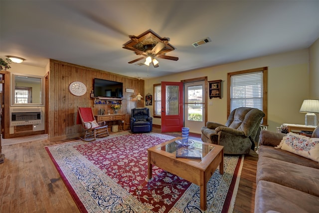 living room featuring wood-type flooring, wood walls, ceiling fan, and heating unit