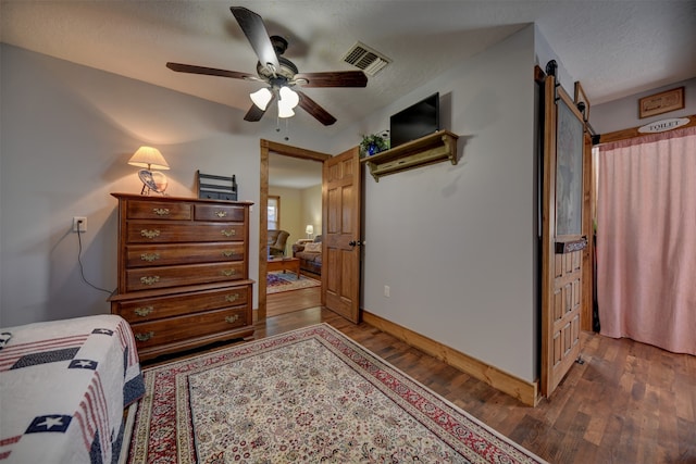 bedroom with ceiling fan, a textured ceiling, dark hardwood / wood-style floors, and a barn door