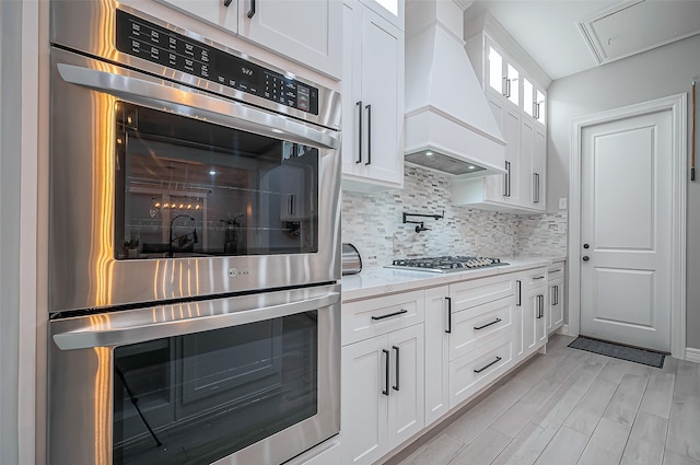 kitchen featuring tasteful backsplash, white cabinetry, stainless steel appliances, and custom range hood