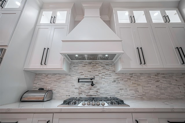 kitchen featuring backsplash, stainless steel gas stovetop, premium range hood, and white cabinetry