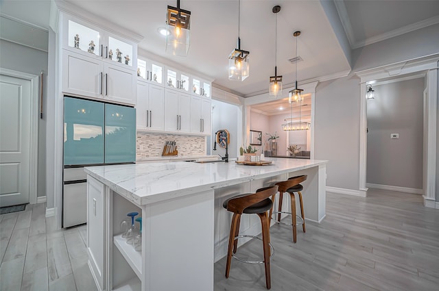 kitchen featuring decorative light fixtures, white cabinets, and an island with sink