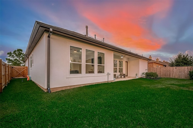 back house at dusk with a lawn and a patio