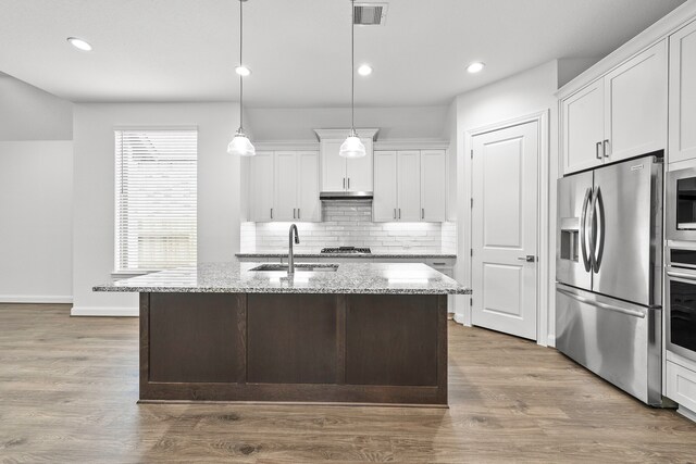 kitchen featuring an island with sink, white cabinetry, light stone countertops, pendant lighting, and stainless steel appliances