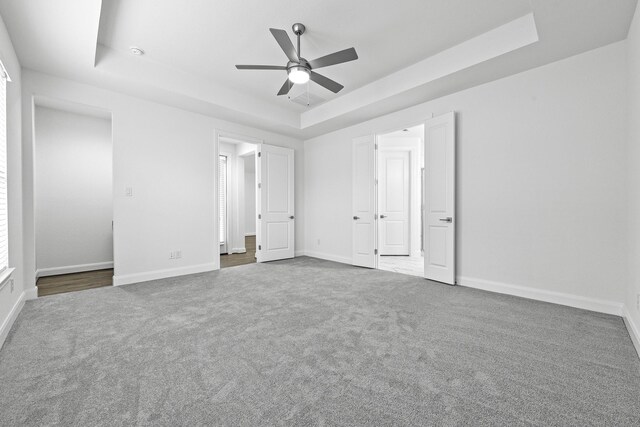 unfurnished bedroom featuring carpet flooring, a tray ceiling, and ceiling fan