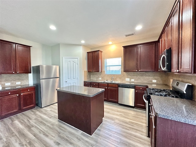 kitchen featuring sink, stainless steel appliances, a center island, dark stone countertops, and light wood-type flooring