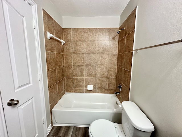 bathroom with a textured ceiling, tiled shower / bath, toilet, and hardwood / wood-style flooring