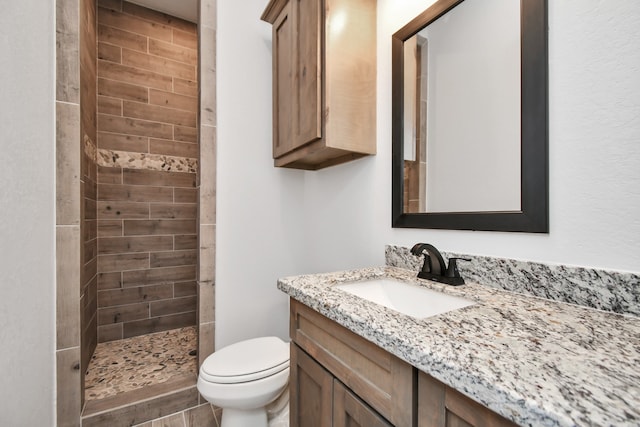 bathroom featuring a tile shower, vanity, and toilet