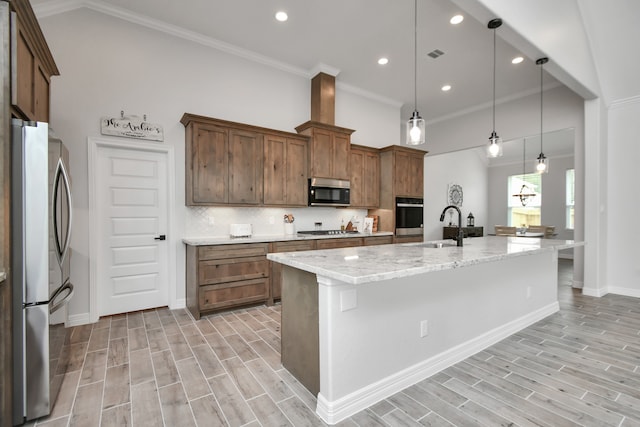 kitchen with light stone counters, stainless steel appliances, light hardwood / wood-style flooring, decorative light fixtures, and a center island with sink