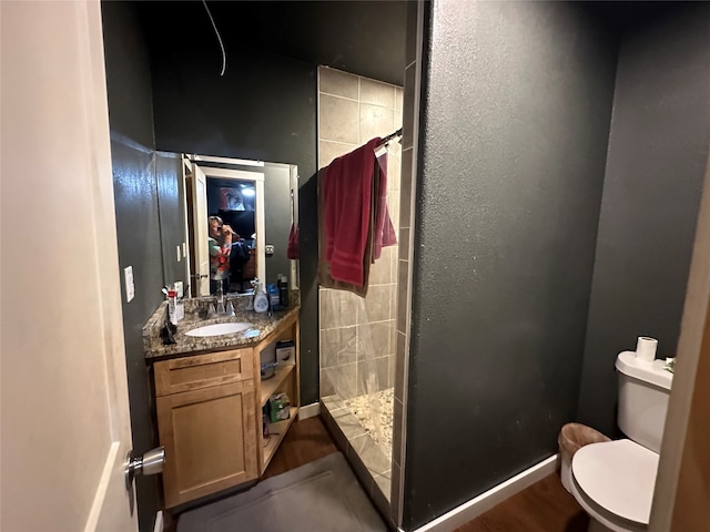 bathroom featuring a tile shower, vanity, toilet, and wood-type flooring