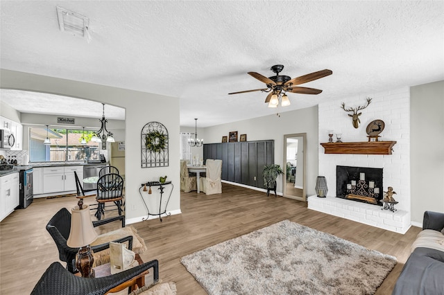 living room featuring ceiling fan with notable chandelier, wood-type flooring, a textured ceiling, and a fireplace