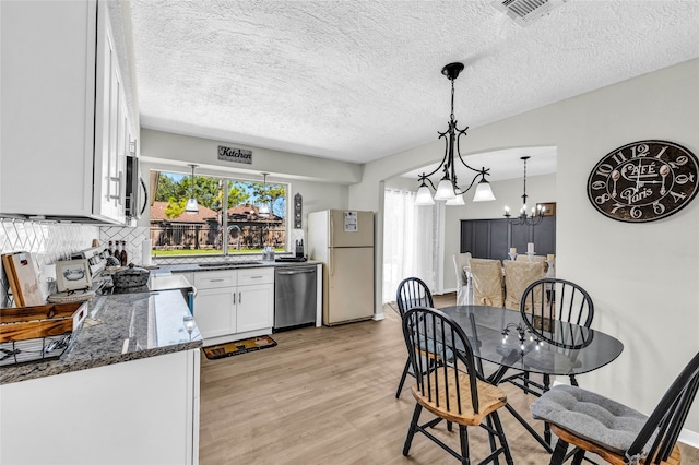 kitchen featuring white cabinets, light hardwood / wood-style flooring, appliances with stainless steel finishes, decorative light fixtures, and dark stone countertops