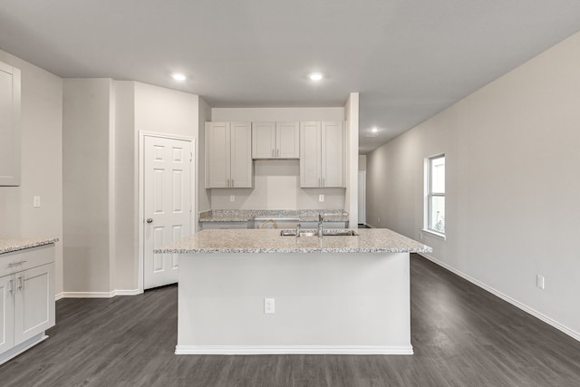 kitchen featuring light stone countertops, a center island with sink, and dark hardwood / wood-style floors