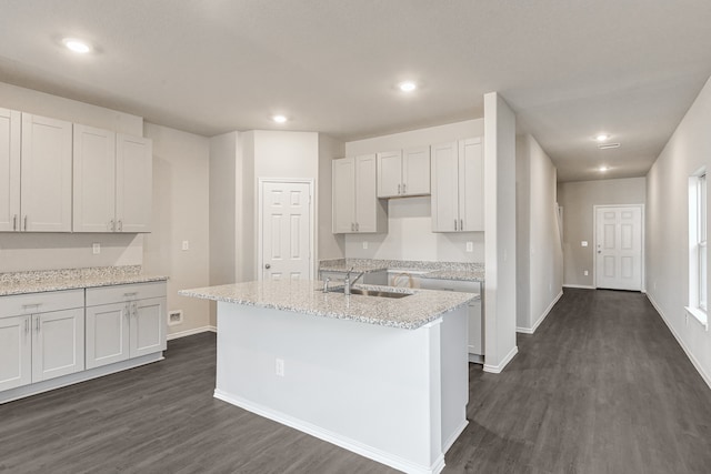 kitchen featuring white cabinets, sink, a center island with sink, light stone countertops, and dark hardwood / wood-style flooring