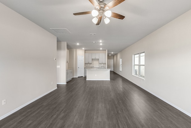 unfurnished living room featuring dark wood-type flooring and ceiling fan