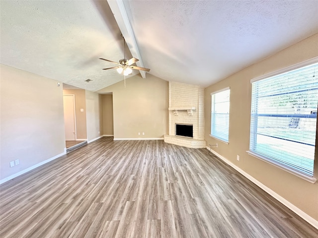 unfurnished living room with a brick fireplace, vaulted ceiling with beams, hardwood / wood-style flooring, and ceiling fan