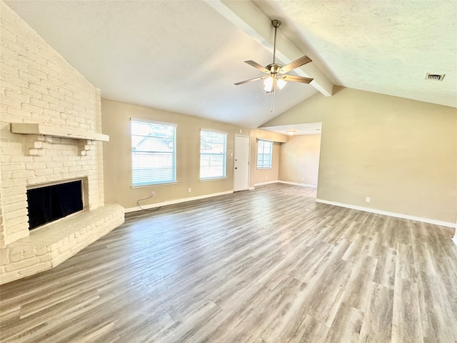 unfurnished living room featuring ceiling fan, a brick fireplace, a textured ceiling, hardwood / wood-style flooring, and lofted ceiling with beams