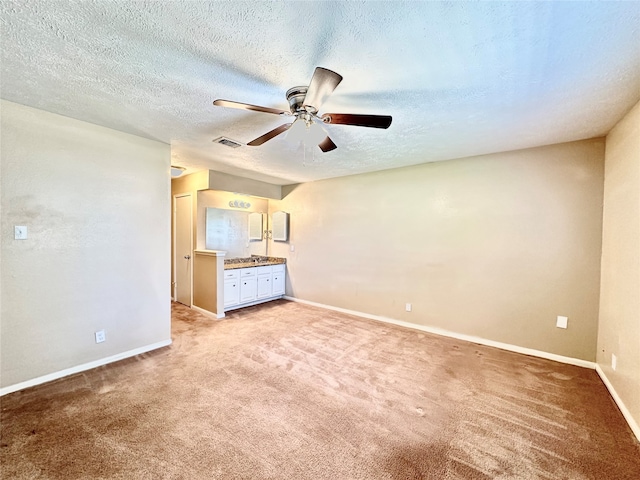 unfurnished bedroom featuring a textured ceiling, connected bathroom, light carpet, and ceiling fan