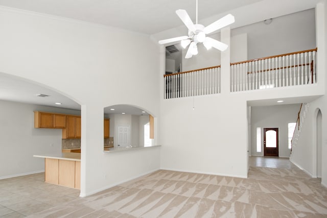 unfurnished living room featuring ceiling fan, a towering ceiling, light tile patterned floors, and crown molding