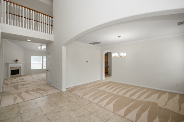 carpeted empty room featuring a towering ceiling, a notable chandelier, crown molding, and a high end fireplace